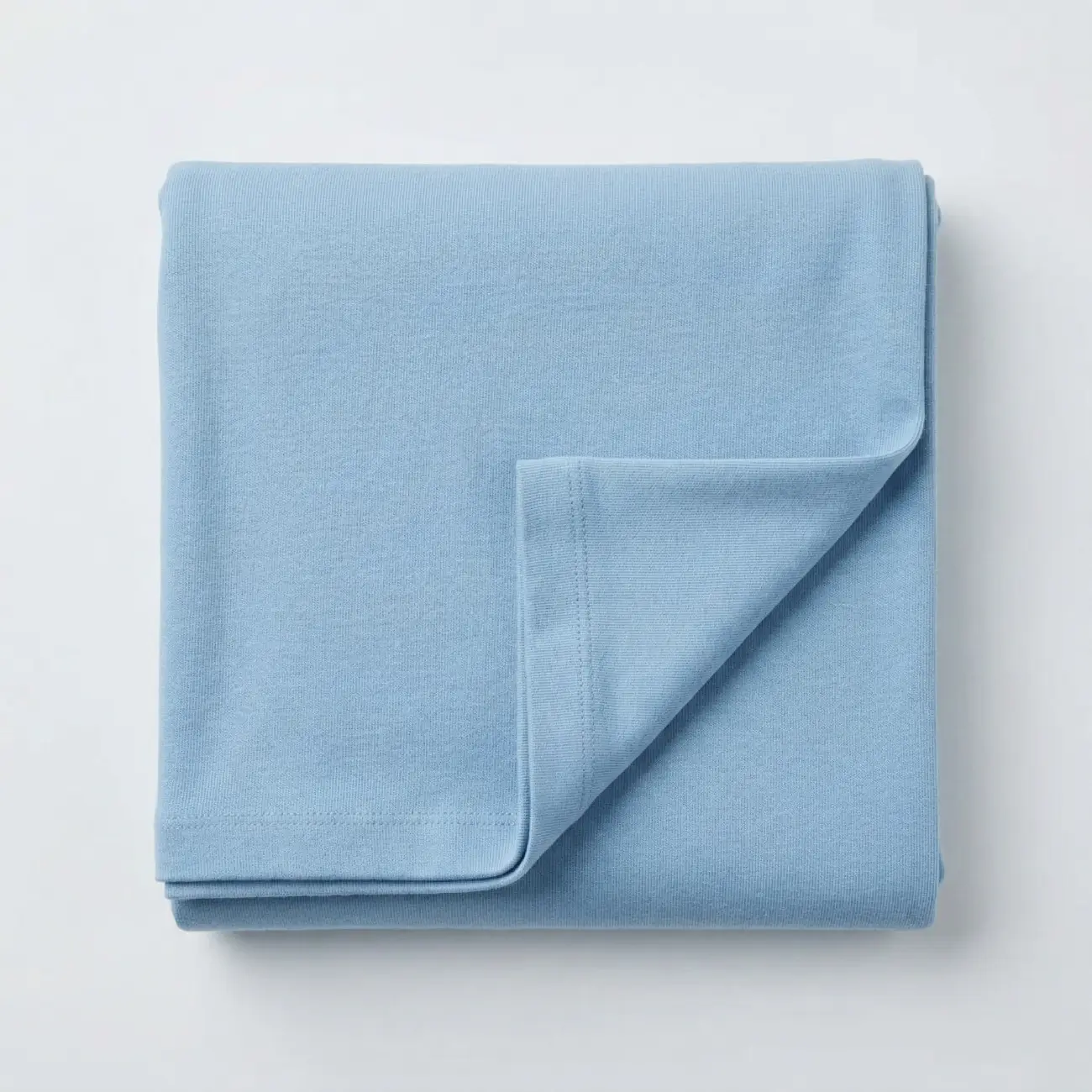 Ein ordentlich zusammengefaltetes Stück hellblauer Bio-Jersey Stoff in der Draufsicht, liegend auf einem hellgrauen Hintergrund.