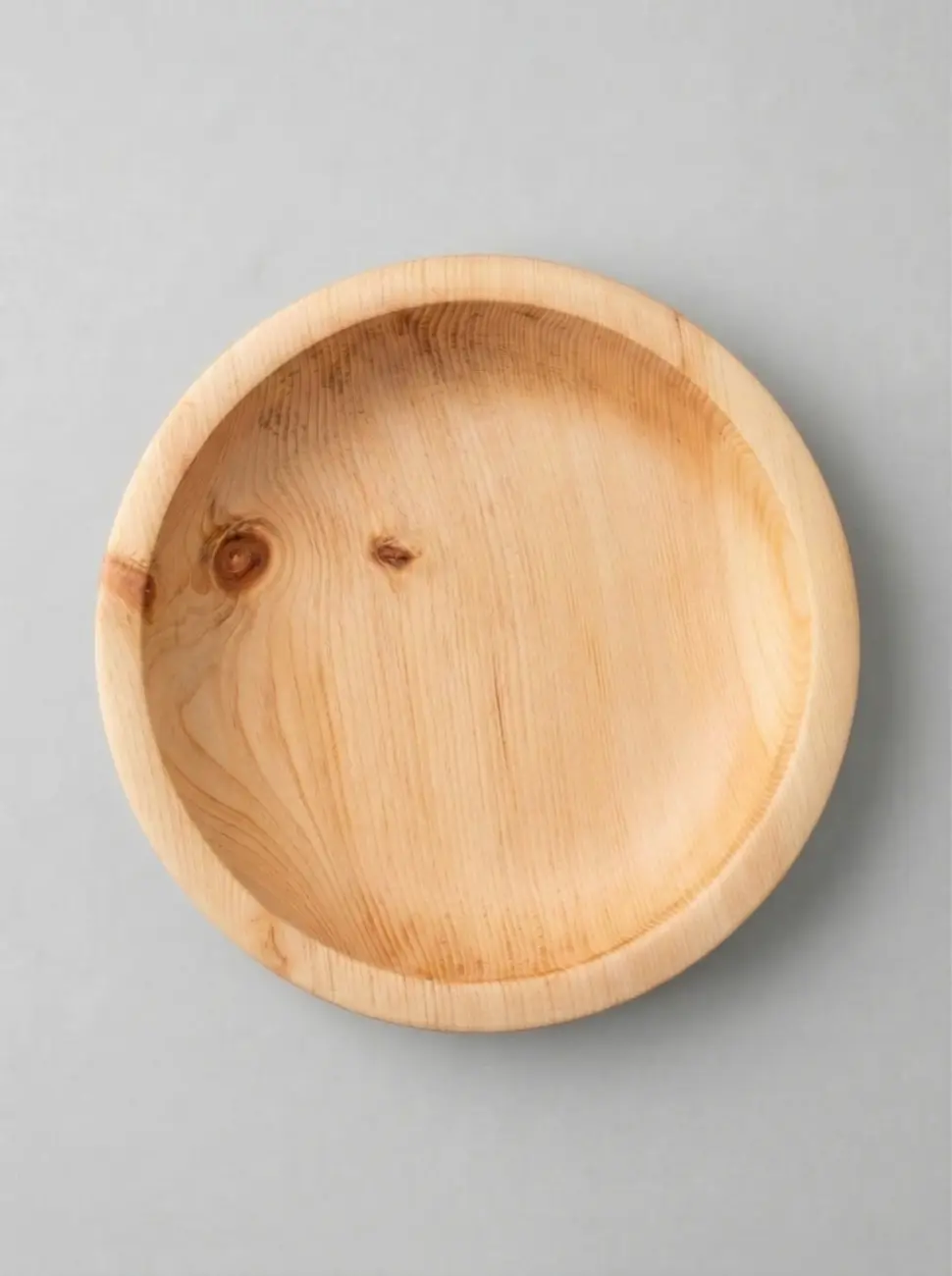 Eine runde, gedrechselte Holzschale (vermutlich aus Zirbenholz) in der direkten Draufsicht auf einem hellgrauen Hintergrund. Das helle Holz zeigt eine markante, natürliche Maserung mit sichtbaren, dunkleren Ästen.