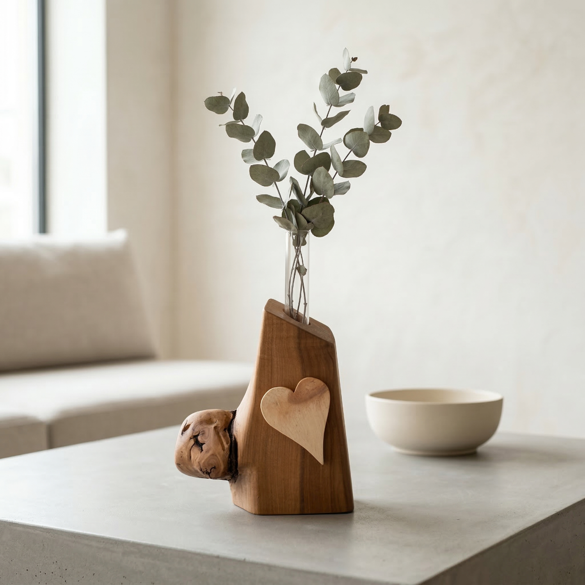 Handgefertigte rustikale Holzvase mit einem hellen Holzherz-Element, dekoriert mit Eukalyptus-Zweigen in einem Glaseinsatz auf einem modernen Tisch in hellem Ambiente.